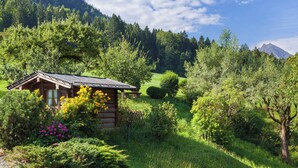 A rustic cabin surrounded by lush greenery and a mountain backdrop. - Ferienwohnung Wiesenblick, für 3-4 Personen (Berchtesgaden)