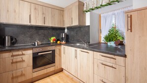 A modern kitchen with wooden cabinets, a built-in oven, a sink, and a countertop with a coffee maker and fresh produce. - Ferienwohnung Wiesenblick, für 3-4 Personen (Berchtesgaden)