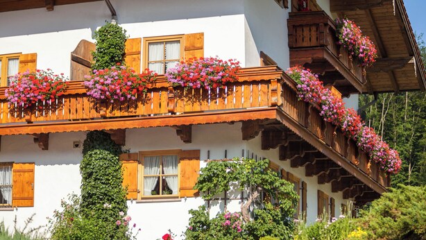 A traditional chalet with wooden balconies adorned with flowers, a white facade, and wooden shutters. - Ferienwohnung Wiesenblick, für 3-4 Personen (Berchtesgaden)