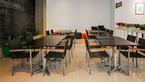 A conference room with multiple tables and chairs, a tiled floor, and a brick wall. - Capital O 93347 Glodok Inn By NAM Near Glodok Plaza (Jakarta)