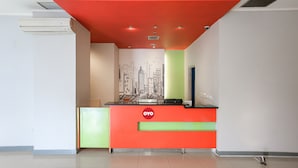 A reception desk with a red and green color scheme, a cityscape mural on the wall, and an air conditioning unit above it. - Capital O 93347 Glodok Inn By NAM Near Glodok Plaza (Jakarta)