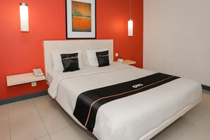 Une chambre d’hôtel avec un lit, une tête de lit blanche, deux oreillers, une table de chevet avec un téléphone et une œuvre d’art accrochée au mur.