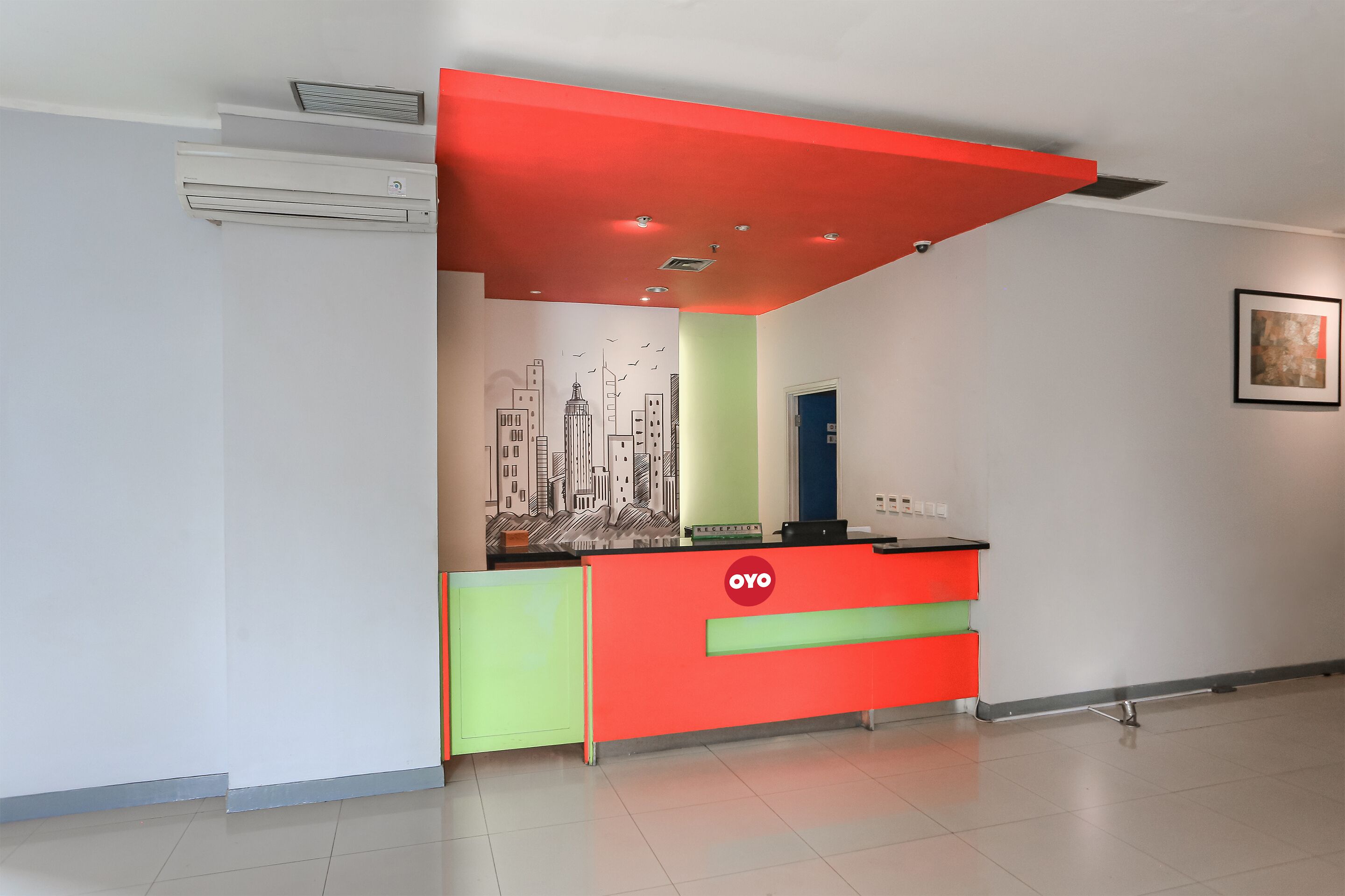 A reception desk with a red and green color scheme, a cityscape mural on the wall, and a framed picture on the wall.