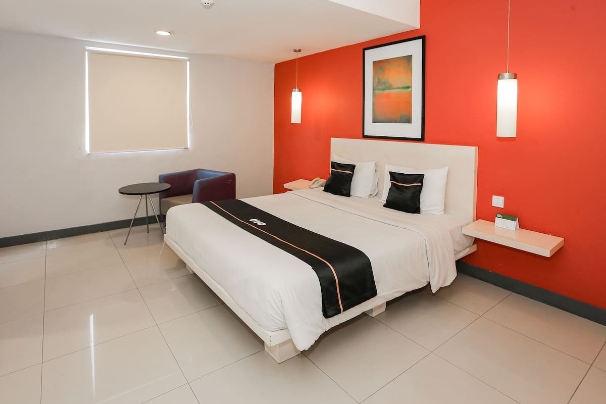 Habitación de hotel moderna con una cama grande, un escritorio pequeño, una silla y una ventana con persianas.