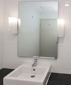 Une salle de bain avec un lavabo blanc, un grand miroir et deux appliques murales.