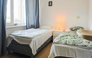 Ein Schlafzimmer mit zwei Betten, einem Nachttisch mit Lampe, einem Fenster mit Vorhängen und einem Wandbild.