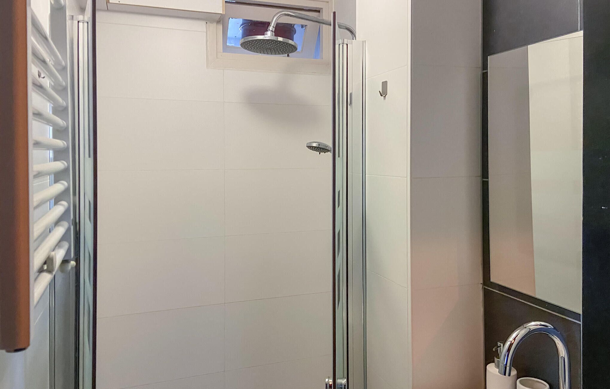 Um chuveiro com proteção de vidro, com um chuveiro manual e um chuveiro fixo.