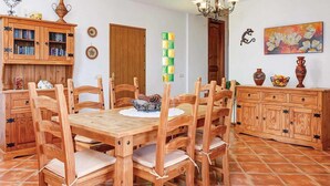 A dining area with a wooden table and chairs, a cabinet with glass doors, and a painting on the wall. - Casa Santiago (Frigiliana)