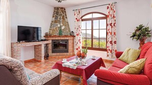 A cozy living room with a fireplace, a television, and a red sofa. - Casa Santiago (Frigiliana)