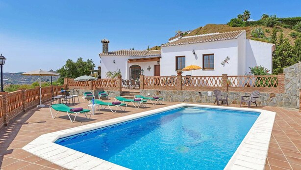 A poolside area with a rectangular pool, lounge chairs, and a white building with a tiled roof. - Casa Santiago (Frigiliana)