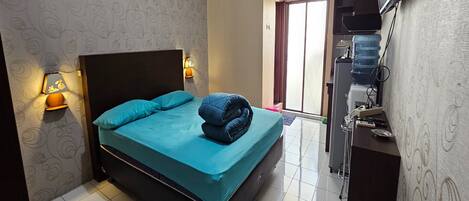 A hotel room with a bed, a desk with a water dispenser, and a TV mounted on the wall.