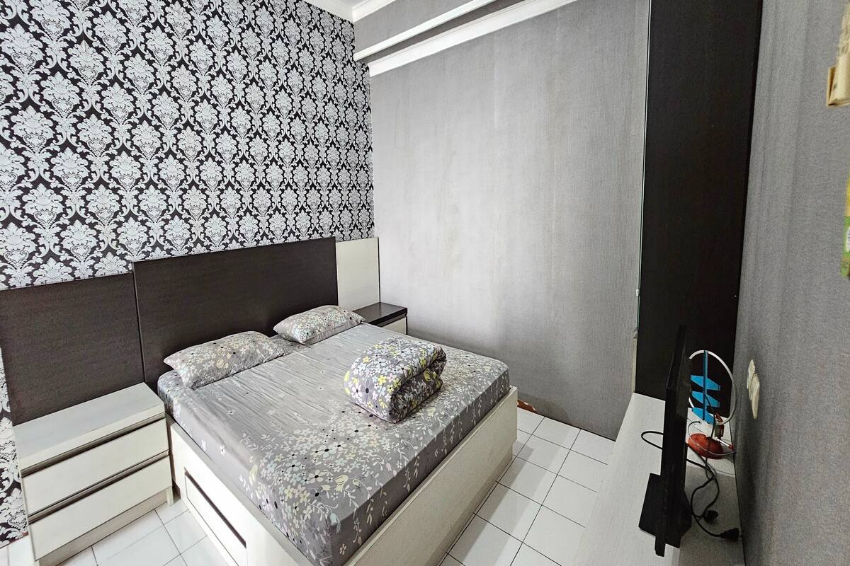 A bedroom with a bed, nightstands, a TV, and patterned wallpaper.