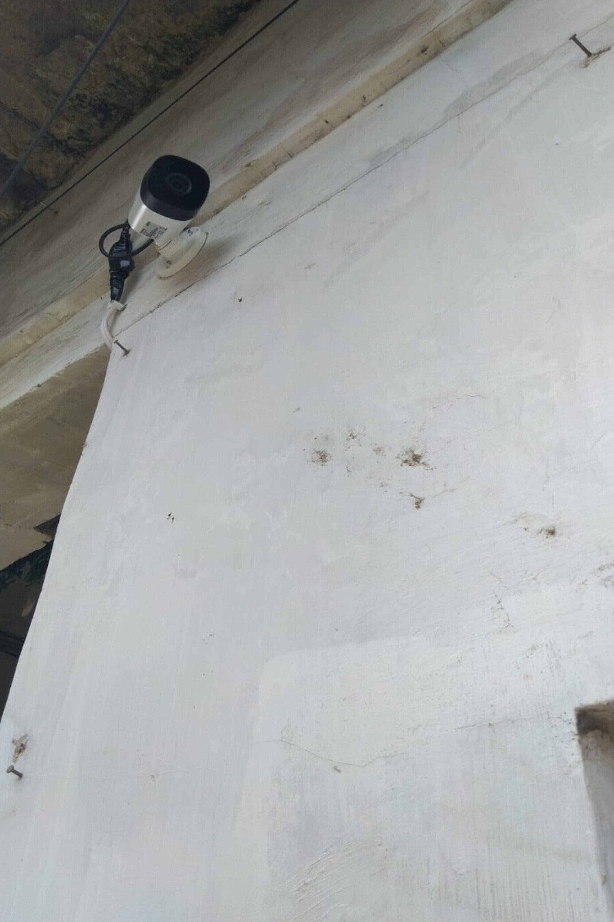 Un mur blanc sur lequel est fixée une caméra de surveillance.