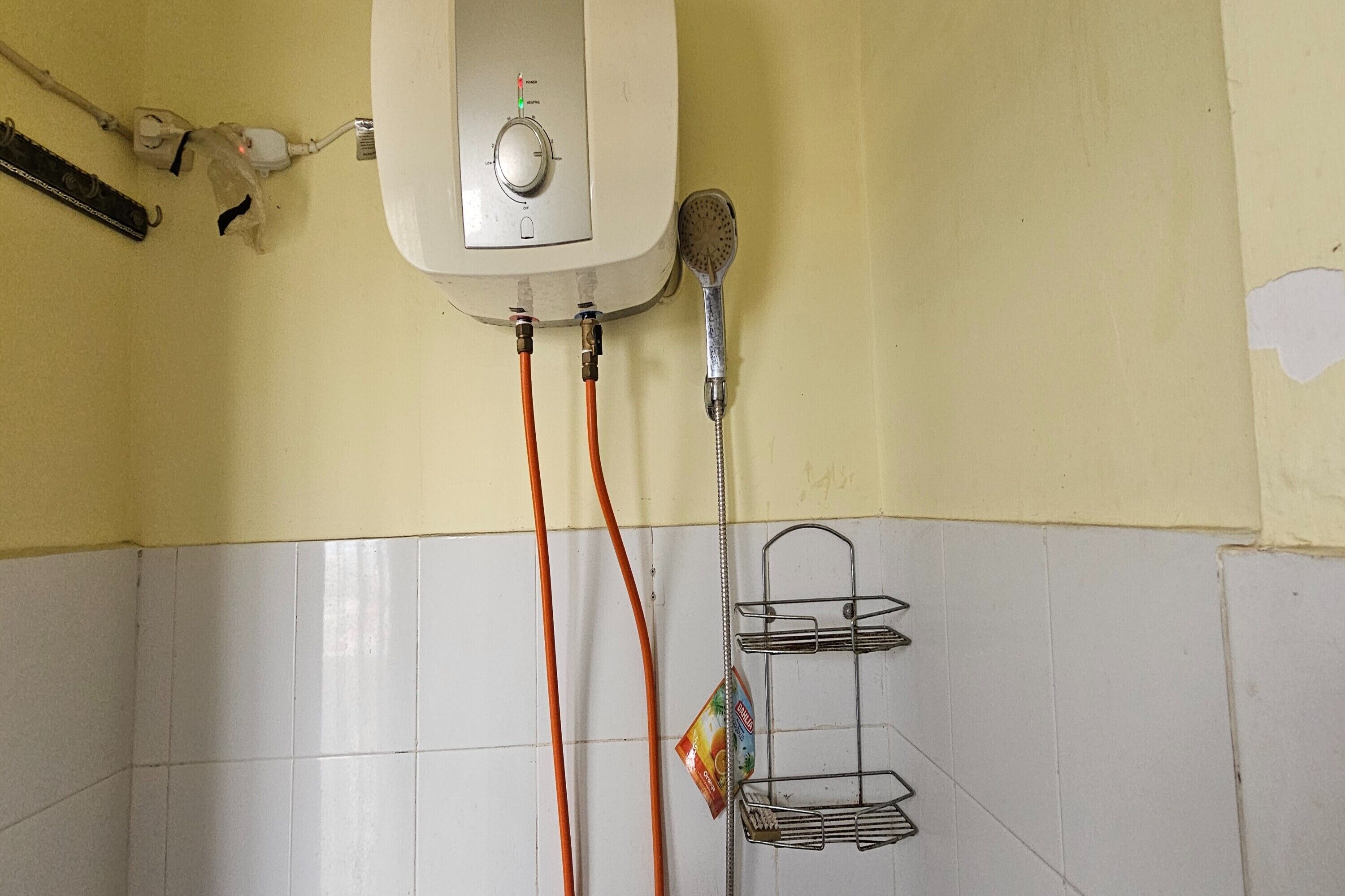 A bathroom with a white tiled wall, a showerhead, and a metal rack.