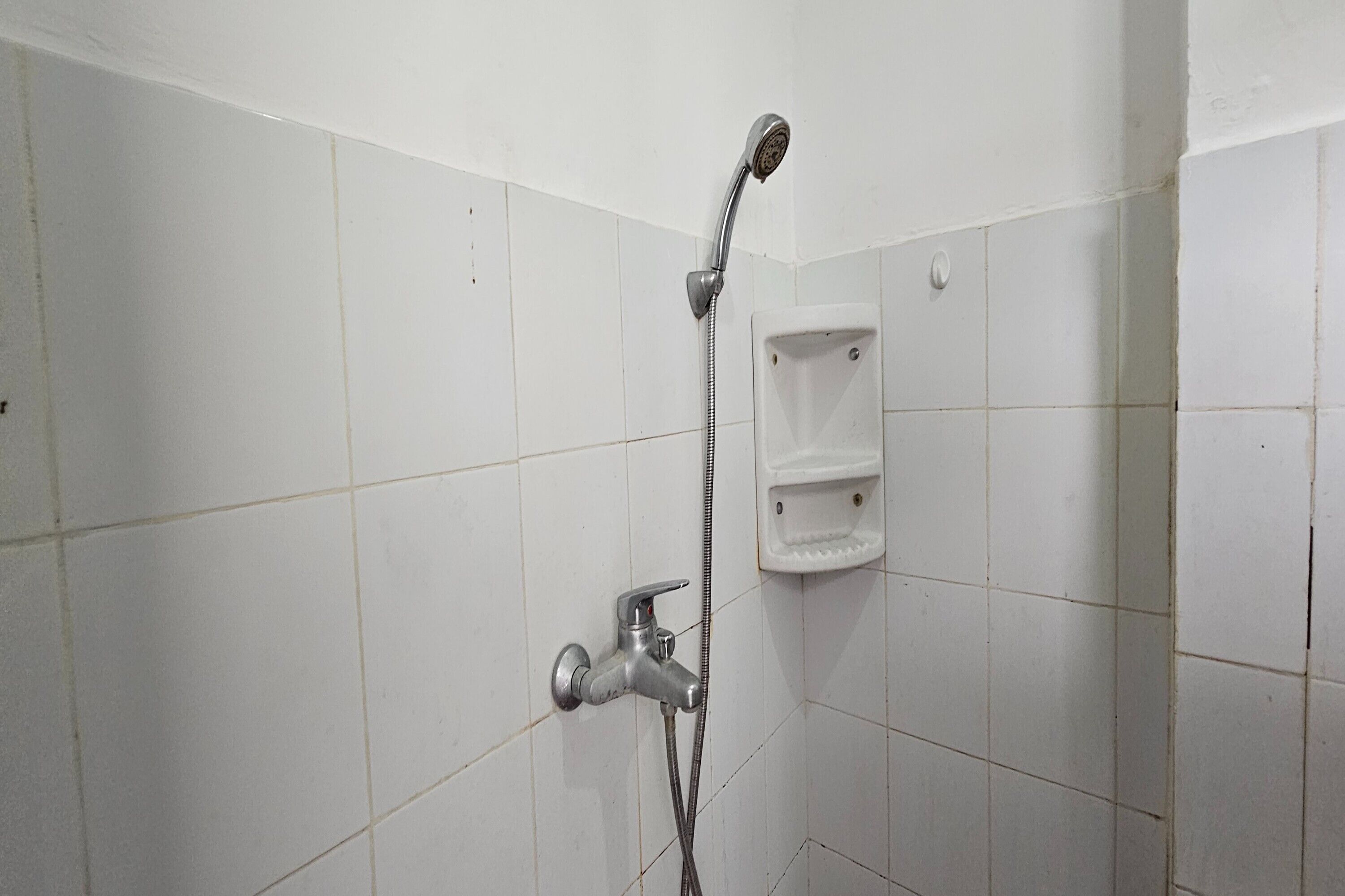Un espacio de ducha con azulejos blancos, un cabezal de ducha de mano y una llave de pared.