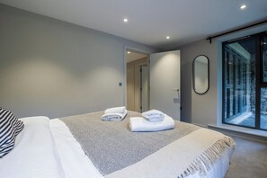 A modern bedroom with a bed, a large mirror, and a view of a stone wall through a glass door. - Quiet 2BR Flat in Backbarrow near Lake Windermere (Backbarrow)
