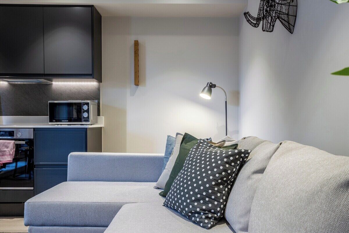 A modern living room with a grey sofa, a microwave, and a small kitchen area.