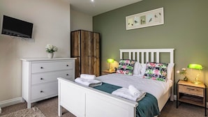 A bedroom with a bed, a dresser, a TV, a wooden wardrobe, and a wall-mounted picture.