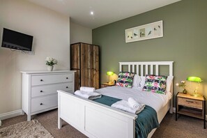 A bedroom with a bed, a dresser, a TV, a wooden wardrobe, and a wall-mounted picture.