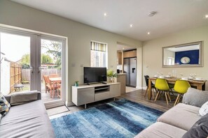 A modern living room with a sofa, a television, a dining area with chairs, and a kitchen in the background. - 4BR in Beeston with Convenient City Centre Access (Beeston)