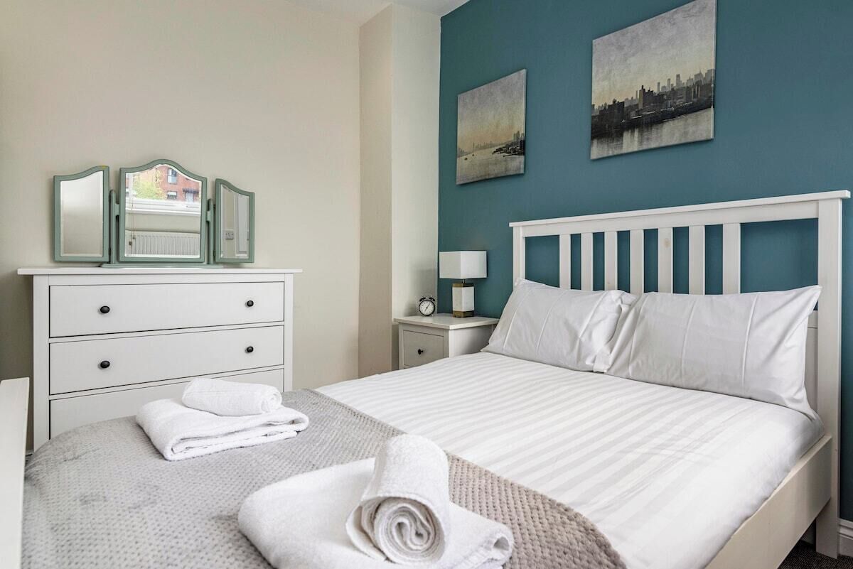 A hotel room with a bed, a dresser with mirrors, a nightstand with a lamp, and two wall-mounted paintings.