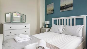 A hotel room with a bed, a dresser with mirrors, a nightstand with a lamp, and two wall-mounted paintings.