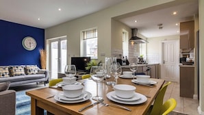 A dining area with a wooden table set for four, a sofa, and a kitchen in the background.