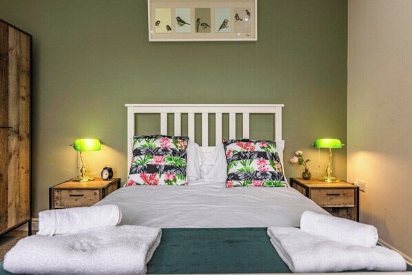 A neatly made bed with white linens, two nightstands with lamps, and a wall-mounted bird illustration.