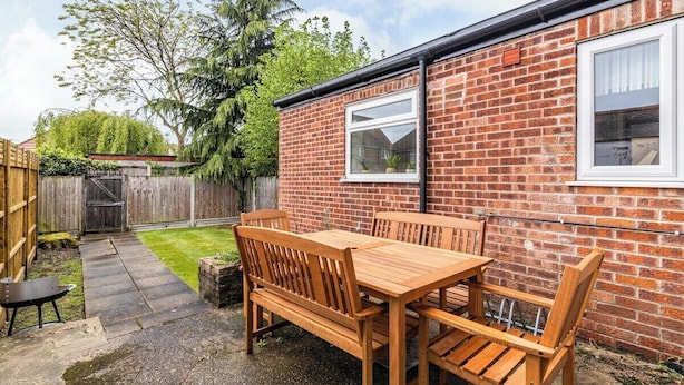 A brick house with a wooden patio, a table, and chairs.