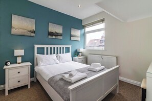 A bedroom with a bed, nightstands, a window, and artwork on the wall.