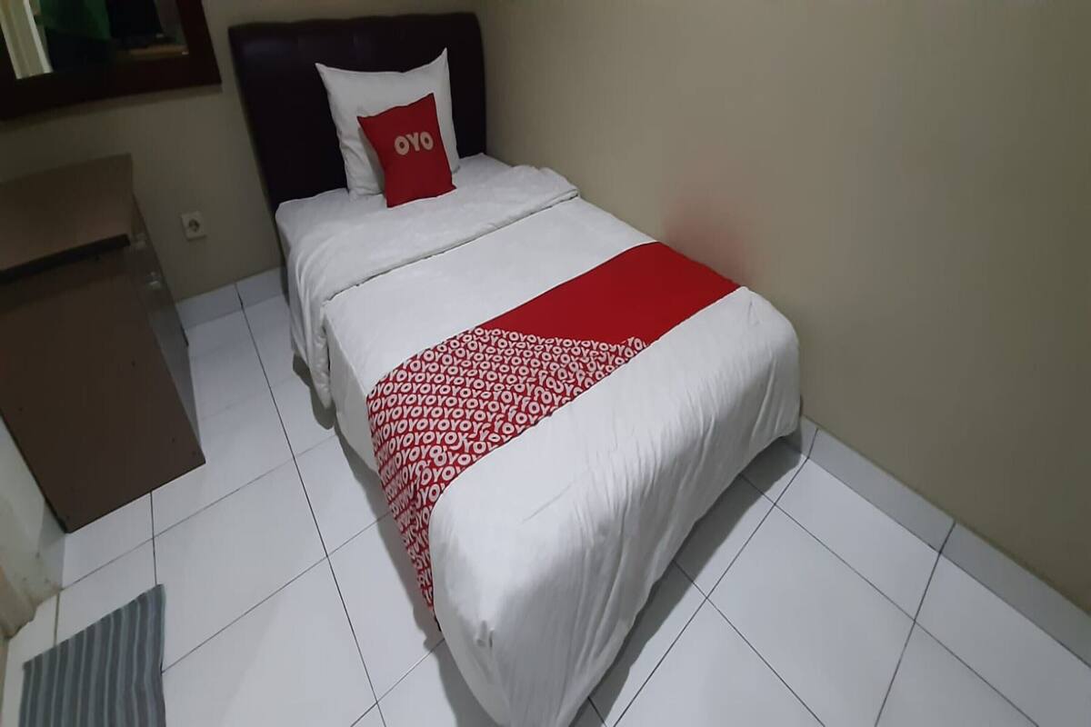 A hotel room with a bed, a red pillow with the word "OYO" on it, a white and red patterned bedspread, and a brown desk.