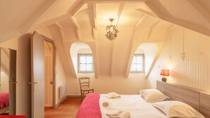 A bedroom with a sloped ceiling, a bed with white linens, a red blanket, a wooden chair, and a small table with a lamp. - Penty Landromiou by Interhome (Crozon-Morgat)