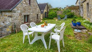 A stone building with a tiled roof, a white table with chairs, and a garden with white flowers. - Penty Landromiou by Interhome (Crozon-Morgat)