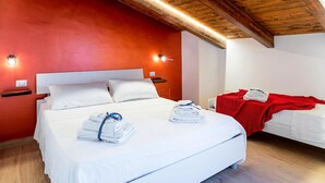 A hotel room with a large bed, a smaller bed, wooden ceiling beams, and a red accent wall. - Cozy home in San Marco Castellabate with WiFi (San Marco Castellabate)