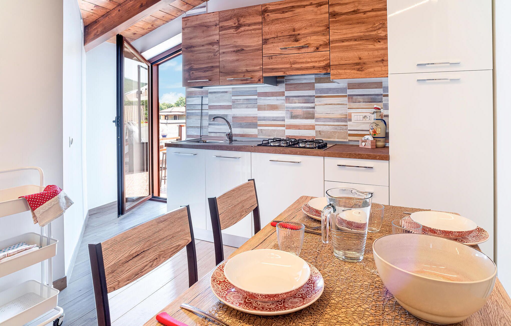 A modern kitchen with wooden cabinets, a tiled backsplash, and a dining area with a table set for two.