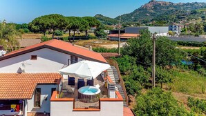 A residential building with a rooftop pool, a terrace with outdoor furniture, and a view of a hillside with houses. - Cozy home in San Marco Castellabate with WiFi (San Marco Castellabate)
