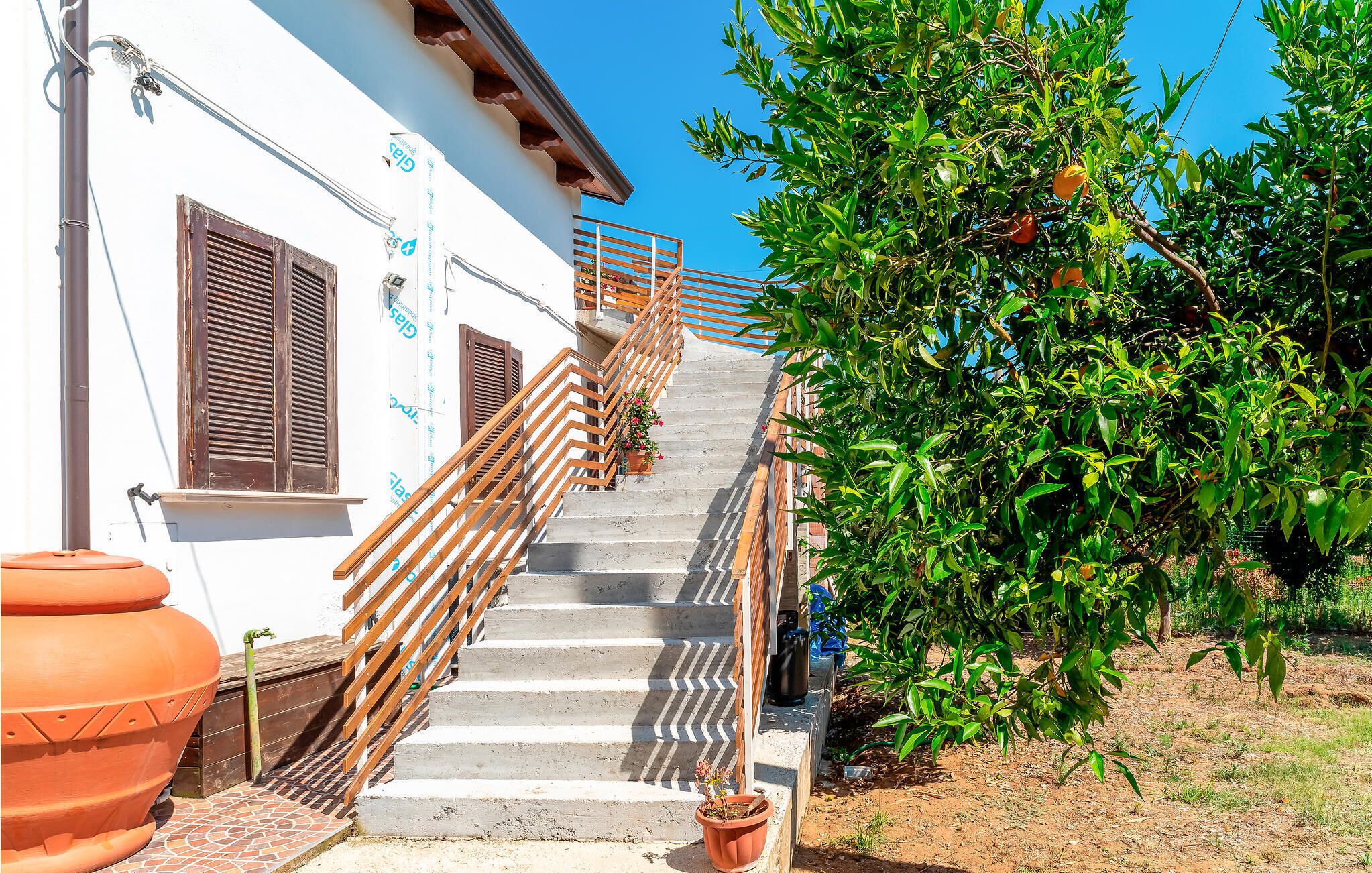 A staircase leading to a white building with wooden railings and a potted plant at the bottom.