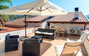 Une terrasse sur le toit, aménagée avec du mobilier d’extérieur, un grand parasol et un chauffe-eau.