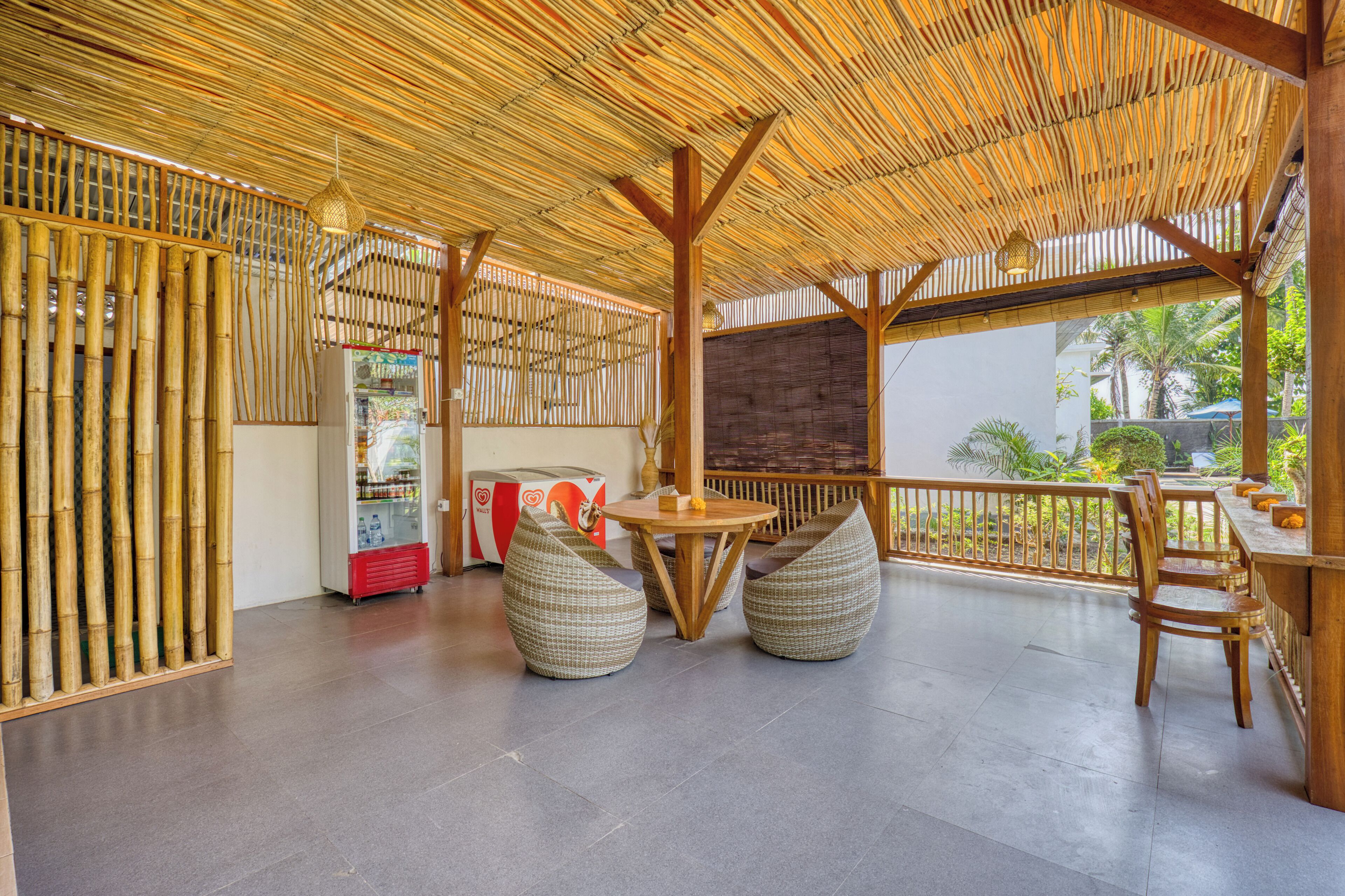A covered outdoor seating area with bamboo walls, a round table, and woven chairs.