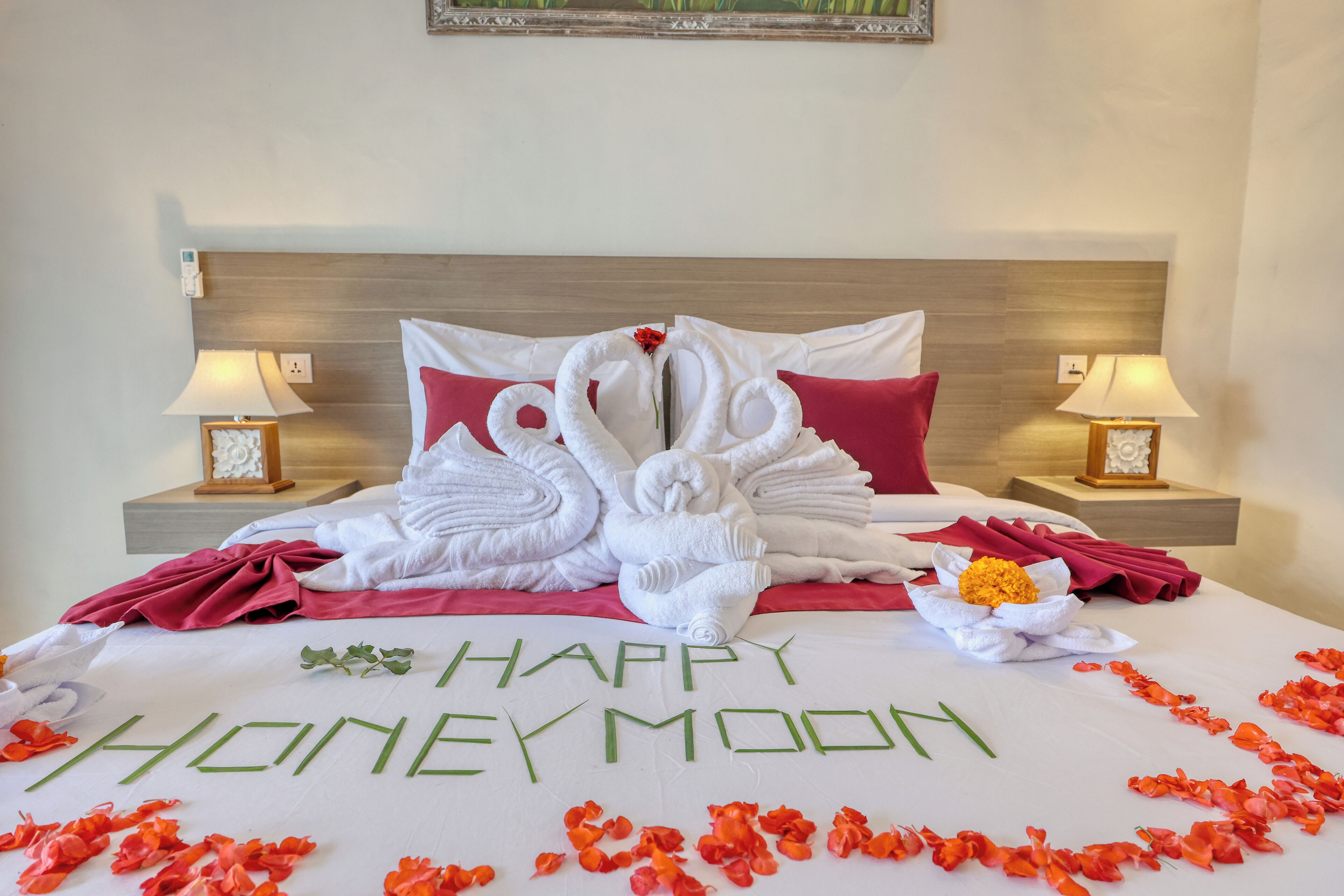 Un lit décoré avec le message « JOYEUSES NOCES », des serviettes en forme de cygne, des oreillers rouges et des pétales de rose éparpillés.