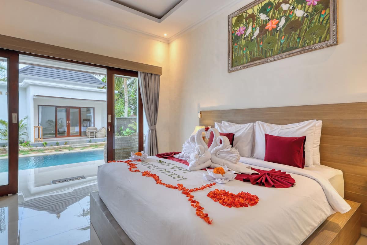 Quarto de hotel com cama, uma pintura e vista para a piscina e um edifício.