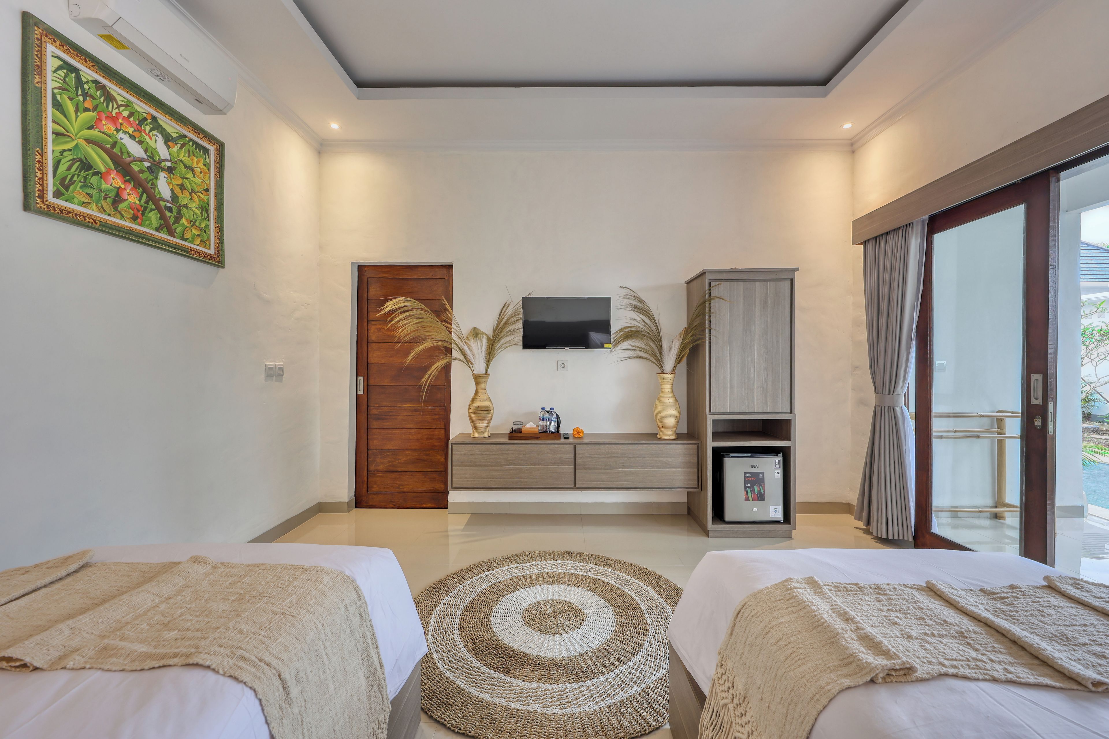 A modern bedroom with two beds, a TV, a cabinet, and a view of the outdoors.