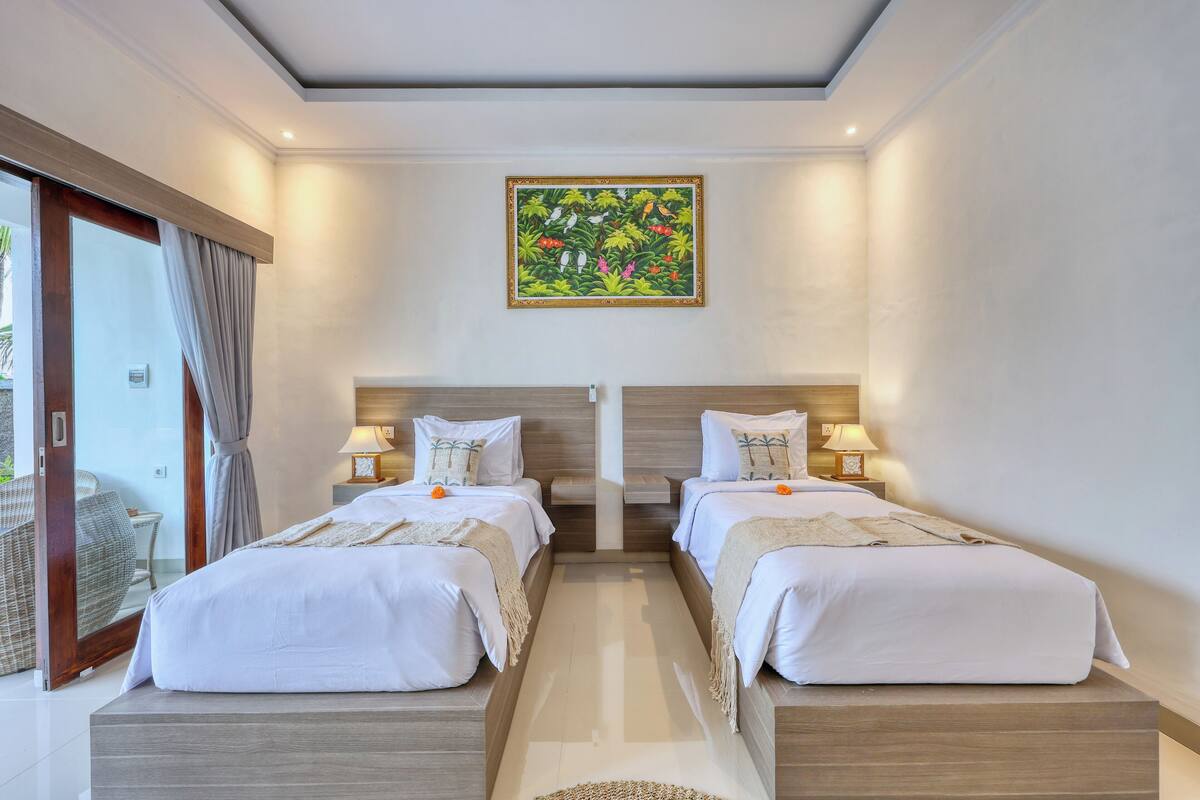 Quarto de hotel com duas camas, uma janela grande e um quadro na parede.