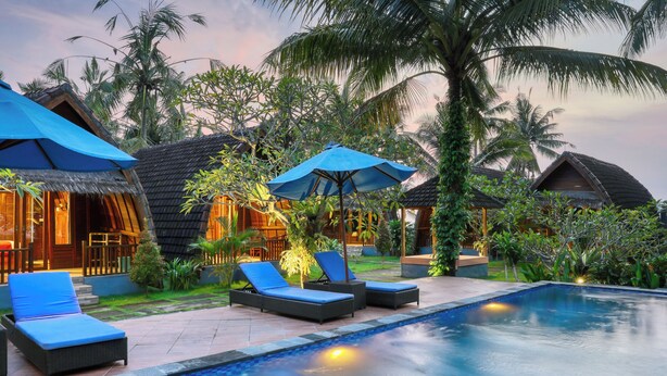 A poolside area with lounge chairs, umbrellas, and thatched-roof structures.