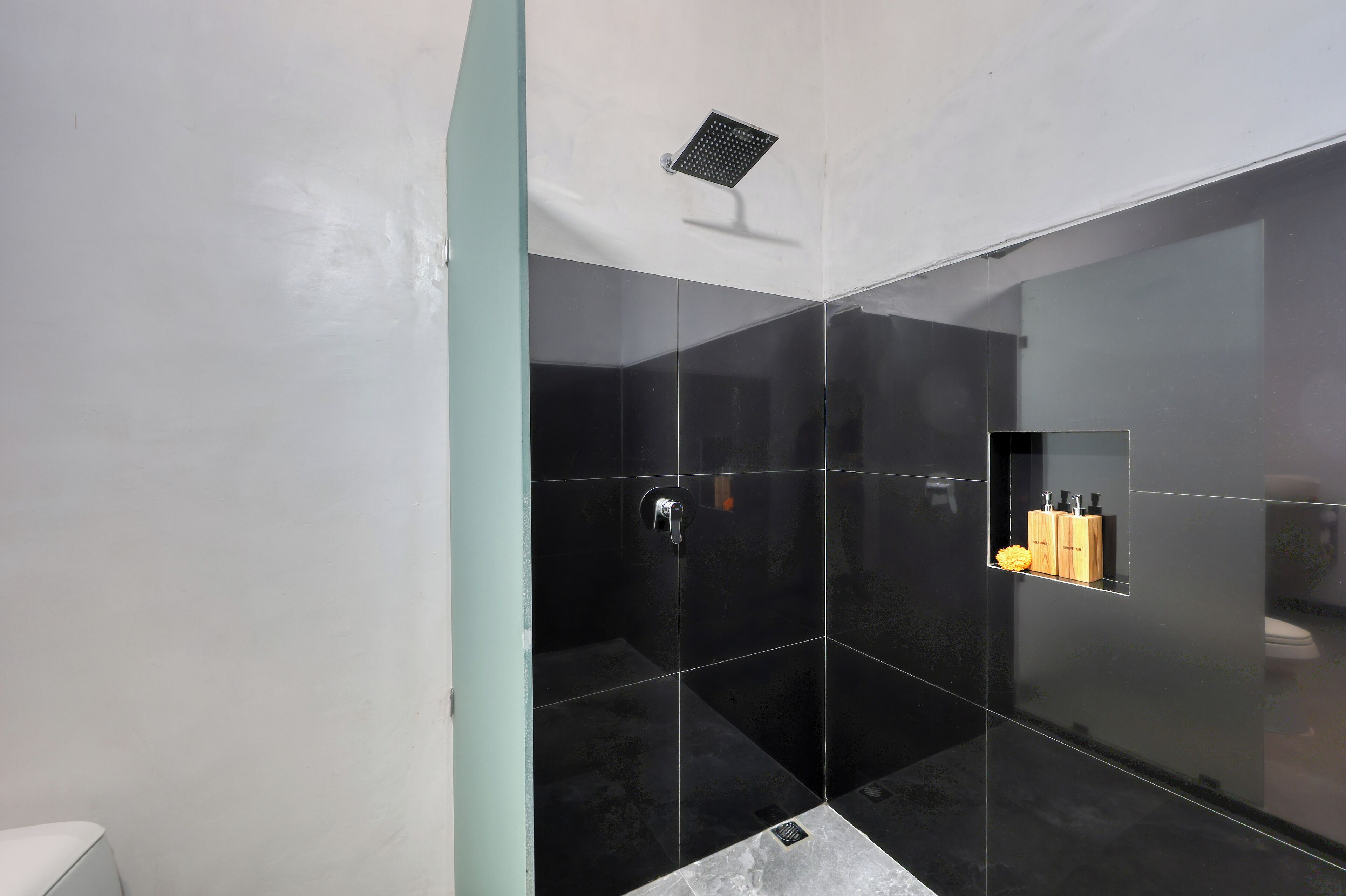 A modern bathroom with black tiles, a showerhead, and a shelf with toiletries.