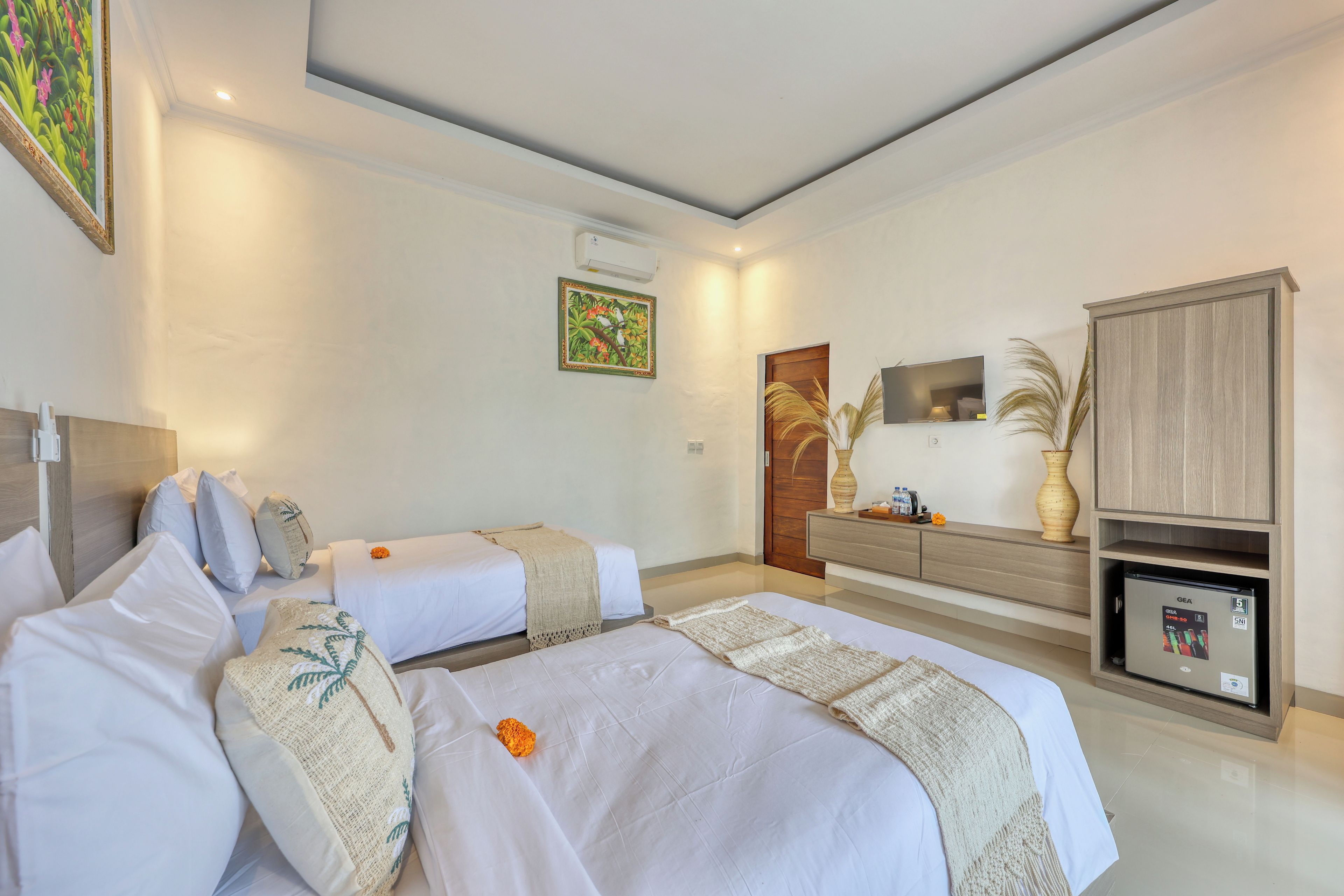 A hotel room with two beds, a wooden cabinet, a TV, and a small refrigerator.