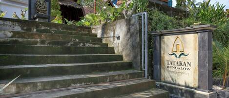 Unos escalones de hormigón conducen a una entrada con portón y un cartel que dice 'TATAKAN BUNGALOW'.