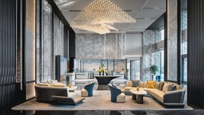 Eine moderne Lobby mit einer Marmor-Rezeption, einem einzigartigen Kronleuchter und einer Sitzecke mit Sofas und einem Couchtisch.