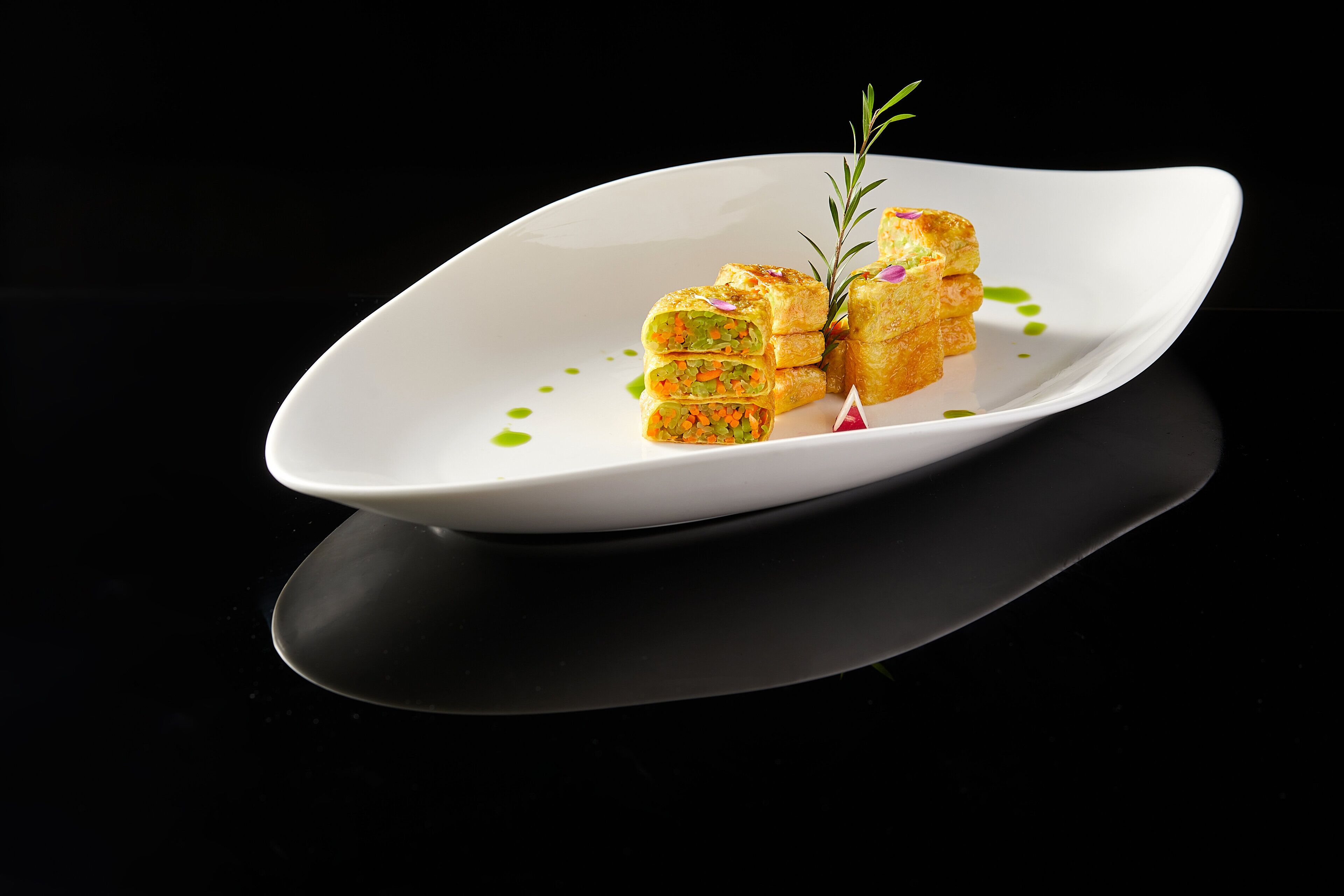 Un piatto bianco con un tovagliolo piegato, guarnito con un rametto di rosmarino, su una superficie nera riflettente.