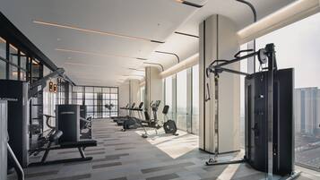 Ett modernt gym med olika typer av träningsutrustning, stora fönster och utsikt över staden.